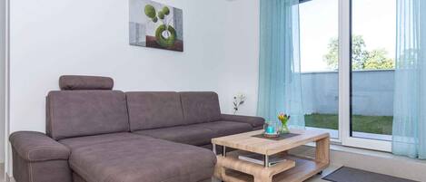 A modern living room with a sectional sofa, a wooden coffee table, and a large window with curtains.