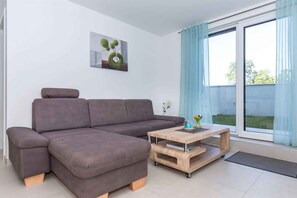 Un salon moderne avec un canapé d’angle, une table basse en bois et une grande fenêtre agrémentée de rideaux.