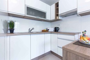 A modern kitchen with white cabinets, a wooden countertop, a sink, a stove, and a plant.