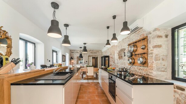 A modern kitchen with a central island, pendant lighting, and a stone accent wall. - Beautiful home in Tkon (Tkon)