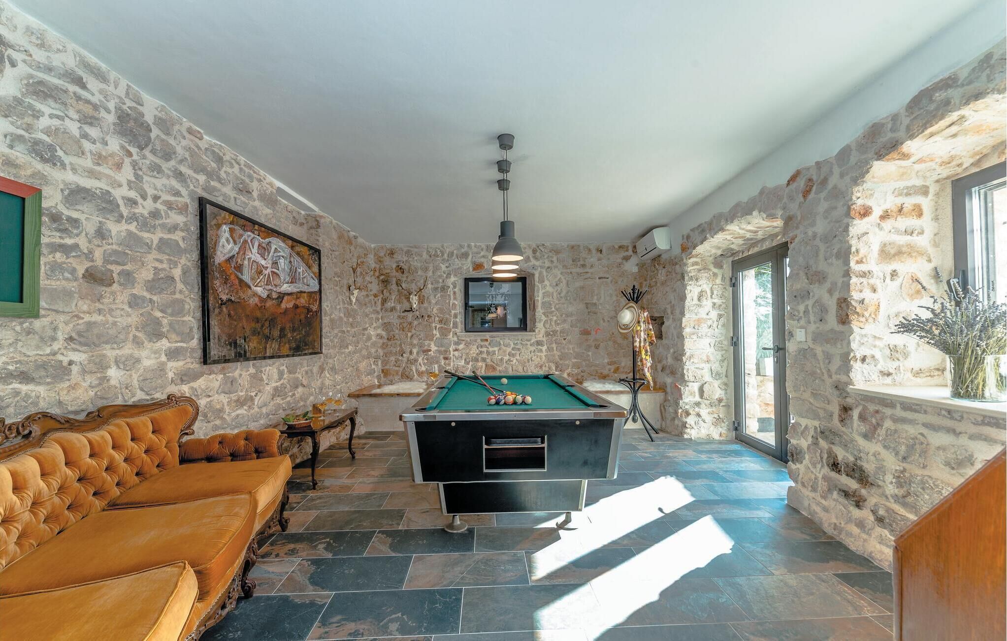 Una habitación con mesa de billar, sofá de cuero, paredes de piedra y un ventanal grande.