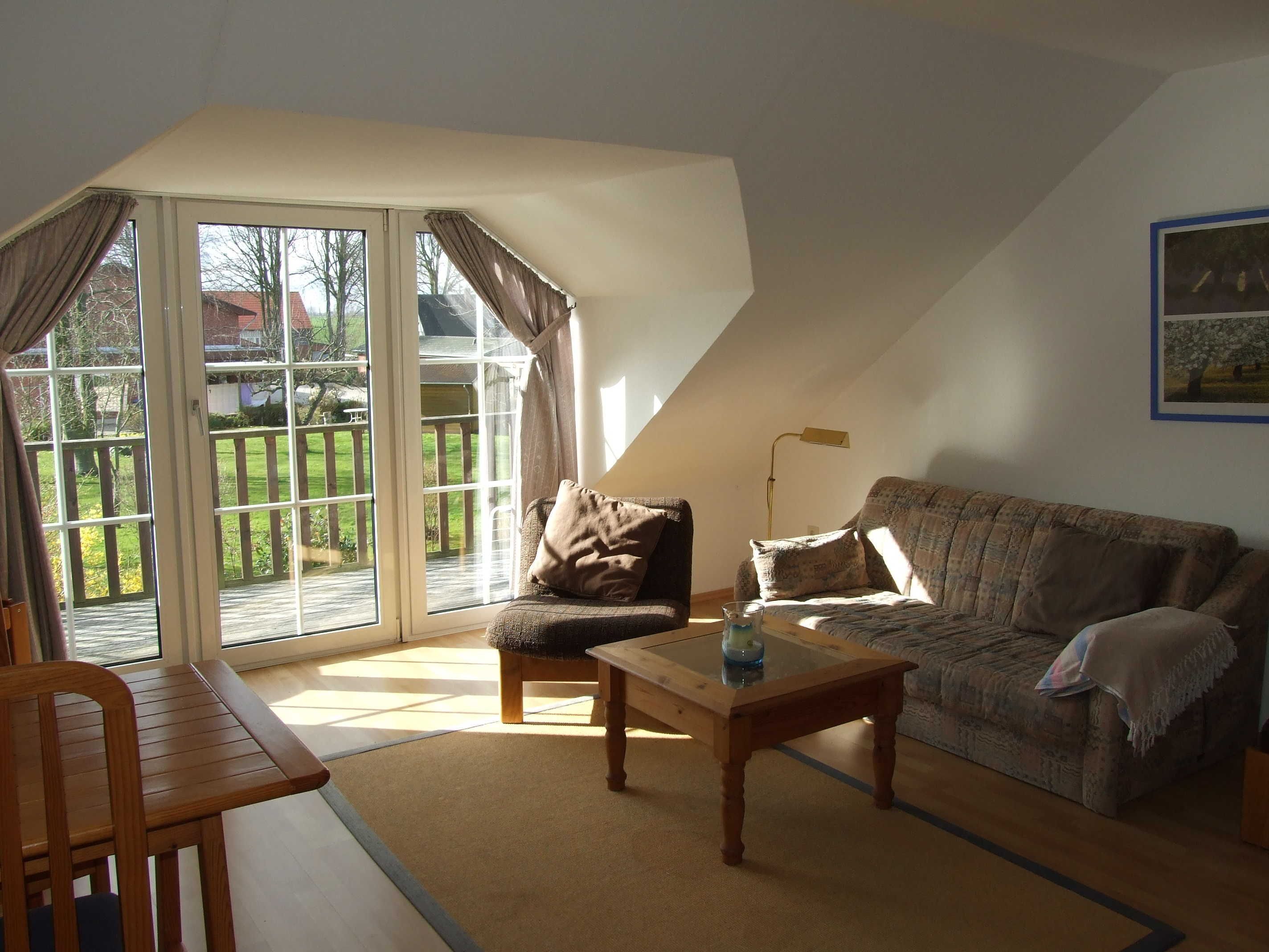 A living room with a sofa, a wooden coffee table, a chair, and a glass door leading to a deck.