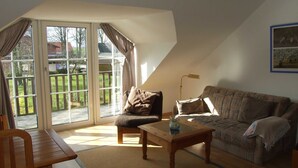 A living room with a sofa, a wooden coffee table, a chair, and a glass door leading to a deck.