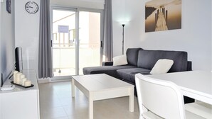 Una sala de estar moderna con un sofá gris, una mesita de centro blanca y un televisor sobre un mueble.