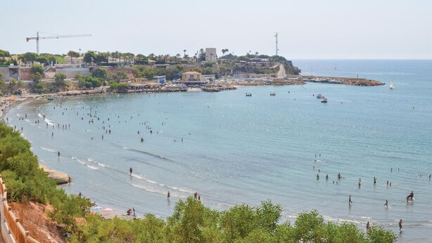Zona costera con playa, embarcaciones y un paisaje urbano distante.