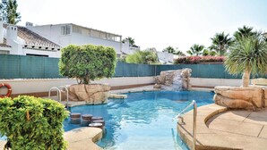 Una piscina con cascada, rodeada de estructuras de piedra y vegetación.
