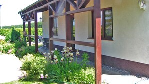 Ein Gebäude mit einer Hollaube, einem Garten mit verschiedenen Pflanzen und Blumen sowie einer Wandleuchte.