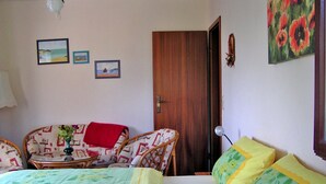 Ein Schlafzimmer mit einem Bett, zwei Stühlen, einem kleinen Tisch mit einer Vase und einer Tür.
