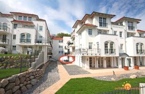Un edificio de varios pisos con fachada blanca y tejas rojas, que cuenta con balcones y una entrada con portón.