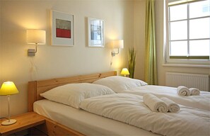 Un lit bien fait, avec du linge de lit blanc, deux lampes fixées au mur et une fenêtre avec des rideaux.