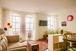 A living room with a sofa, a coffee table, a TV, and a dining area with chairs.