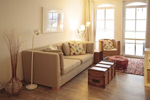Una sala de estar con sofá, sillón, lámpara de pie, un jarrón y un cofre de madera.