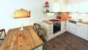 Une cuisine de taille réduite avec des meubles blancs, une table à manger en bois et un luminaire suspendu.