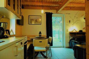 Una cocina con una mesa de comedor, sillas, una lámpara colgante y vistas a través de una puerta.