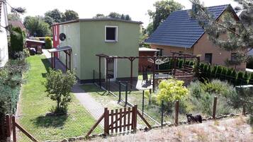 Ein eingezäunter Garten mit einem kleinen Gebäude, einer Holzterrasse und einem Hund.