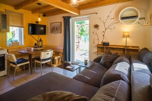 Ein gemütliches Wohnzimmer mit einer Couch, einem Esstisch mit Stühlen, einem an der Wand montierten Fernseher und einem Fenster mit Jalousien.