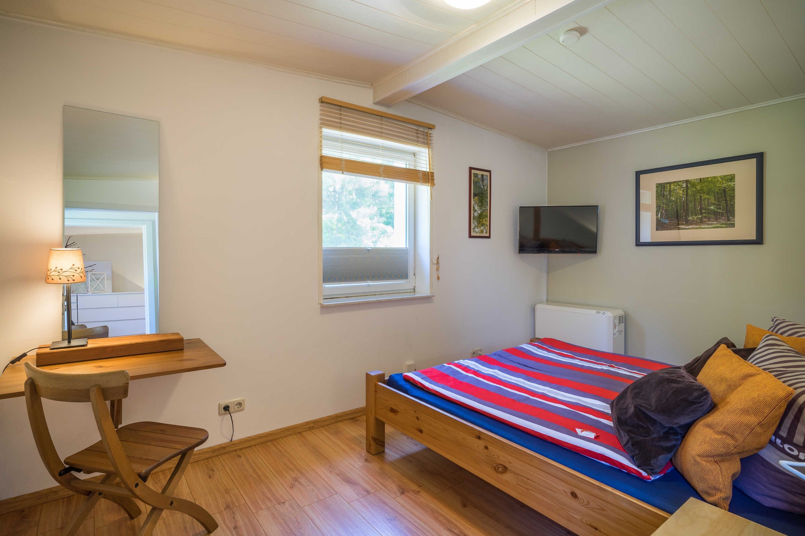 Ein Schlafzimmer mit Bett, Schreibtisch, Stuhl, Fernseher und einem Fenster mit Jalousien.