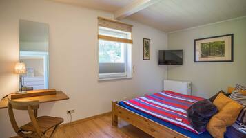 Ein Schlafzimmer mit Bett, Schreibtisch, Stuhl, Fernseher und einem Fenster mit Jalousien.