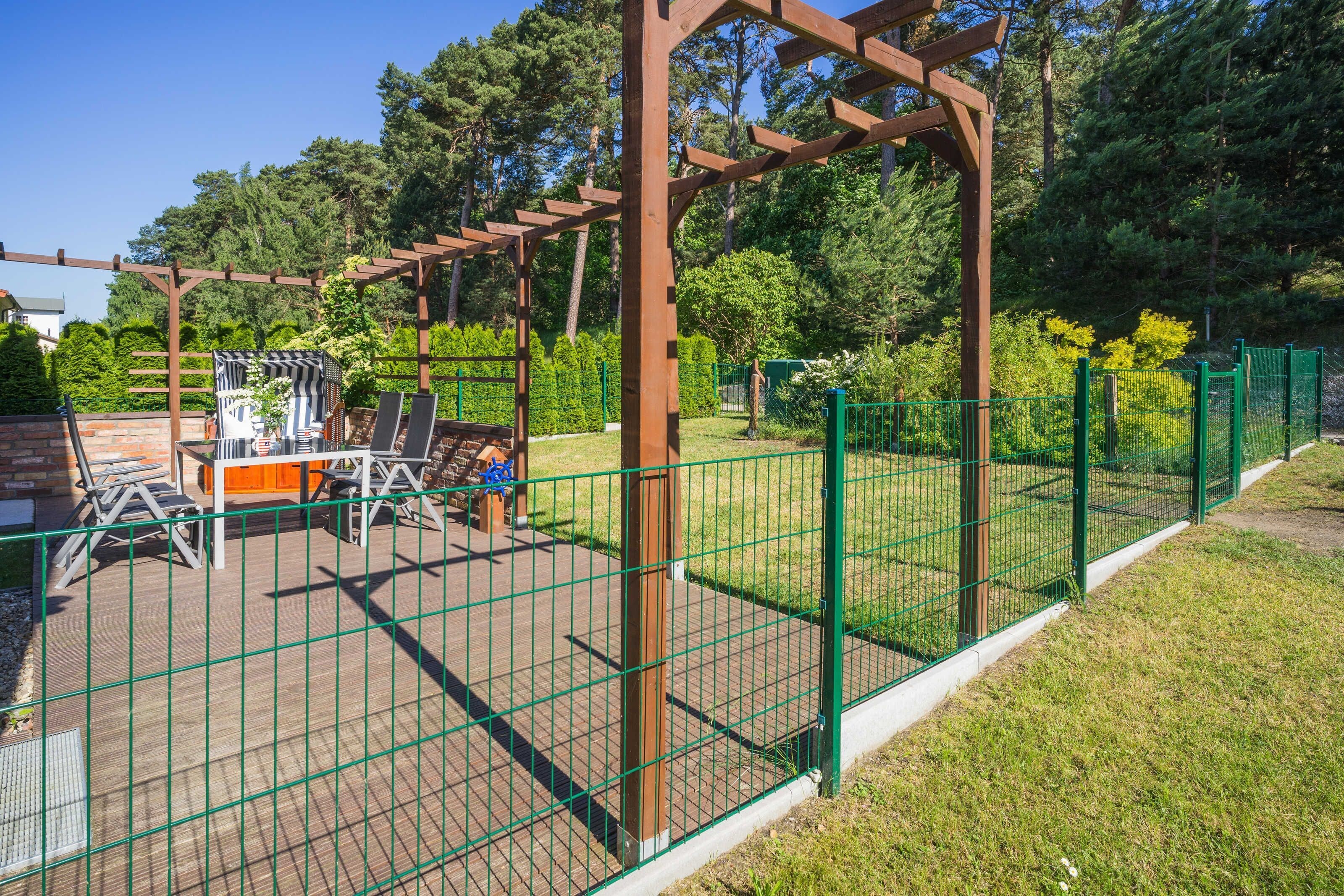 Ein umzäunter Außenbereich mit einer Pergola, Sitzgelegenheiten und einer kleinen Spielanlage.