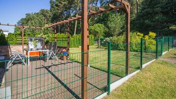 Ein umzäunter Außenbereich mit einer Pergola, Sitzgelegenheiten und einer kleinen Spielanlage.