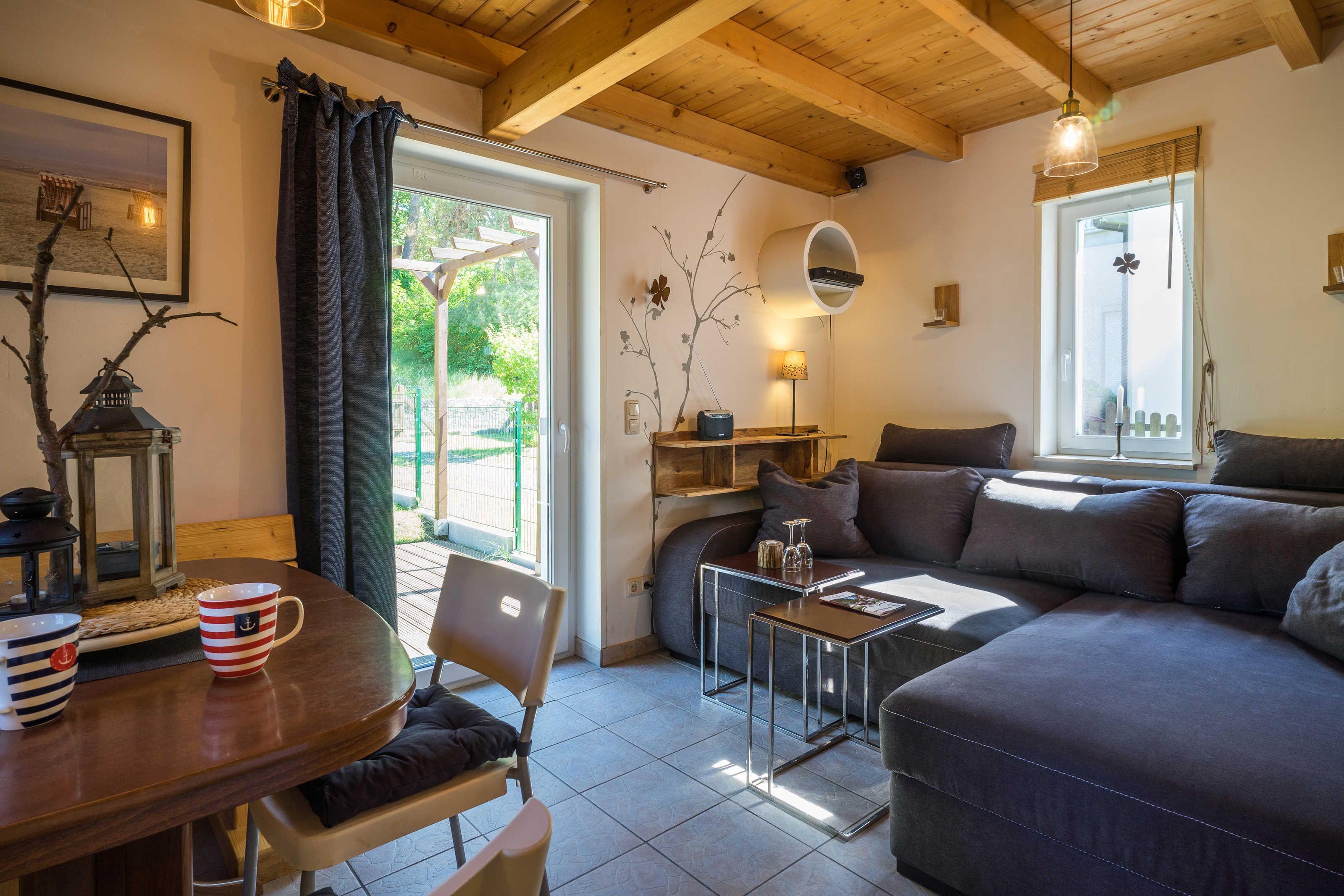 Ein gemütliches Wohnzimmer mit Sofa, Esstisch und Couchtisch. Ein Fenster bietet Blick auf grüne Vegetation.