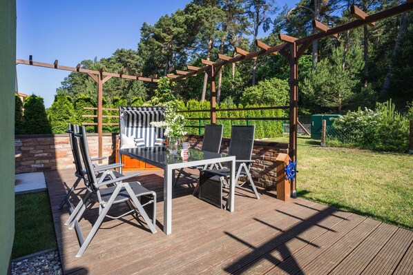 Un patio al aire libre con un pérgola de madera, una mesa de vidrio y sillas de metal.