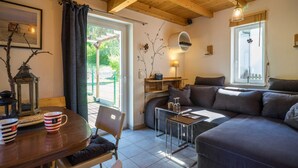 A cozy living room with a sofa, a dining table, and a coffee table. There is a window with a view of greenery outside.