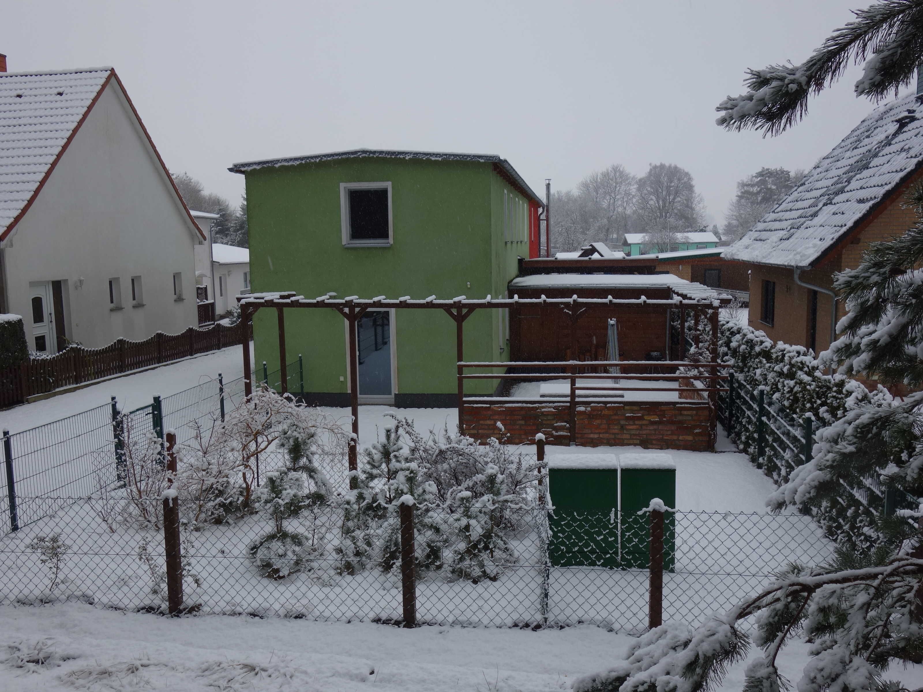 A residential area with houses, a green building, and a snow-covered landscape.