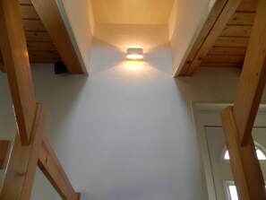 A high ceiling with wooden beams, a central light fixture, and a door at the end.