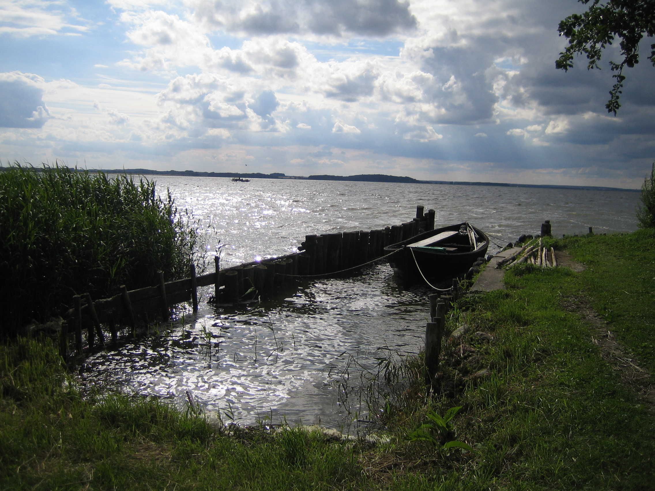 Cuerpo de agua tranquilo con un muelle de madera y un bote amarrado.