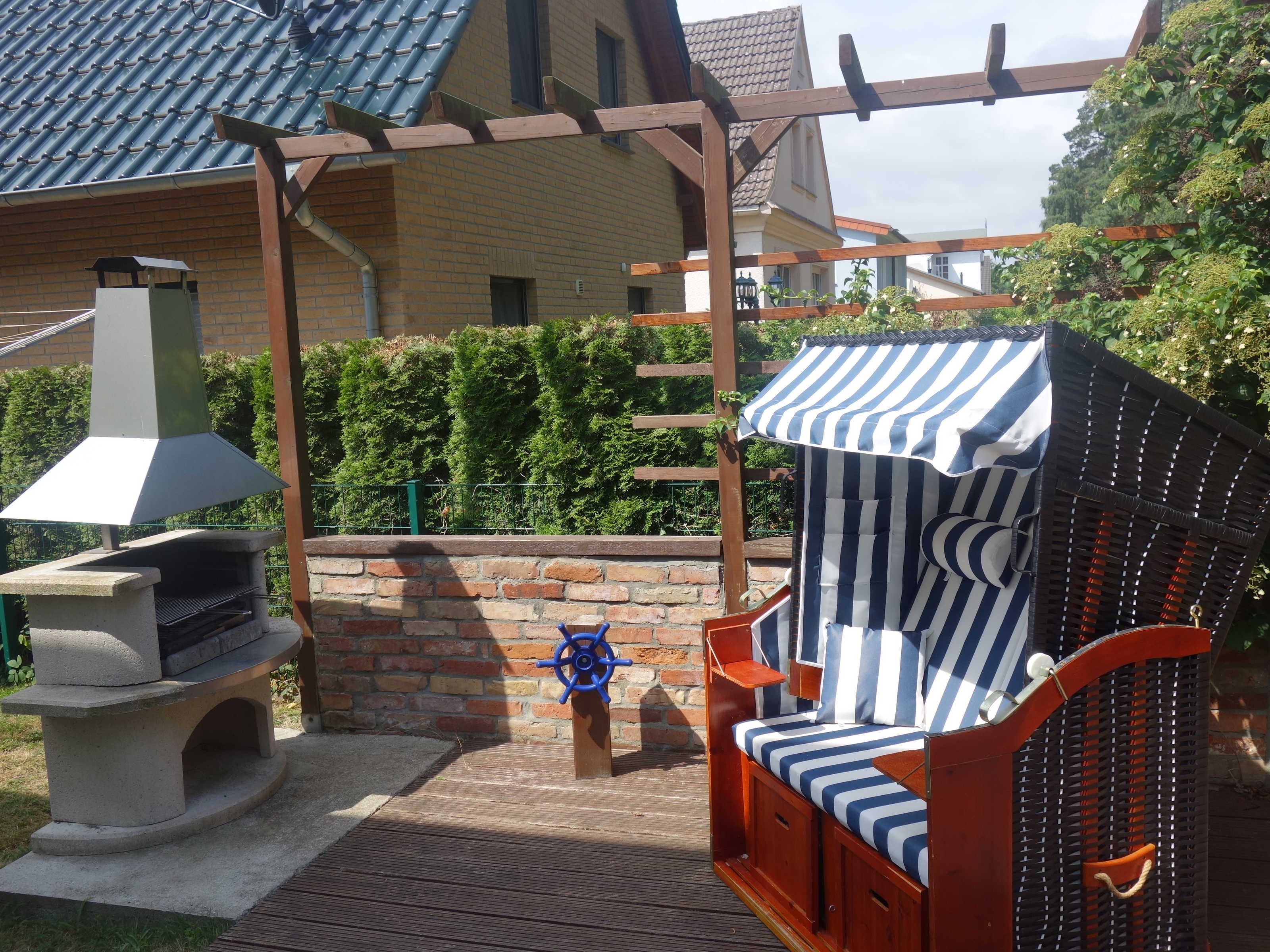 A patio with a grill, a wooden bench with a striped cover, and a pergola structure.