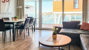 A modern living room with a dining area, a sofa, a coffee table, and a view of a balcony with a railing. - Priwallpromenade 23, Whg 6 (Travemünde Waterfront)