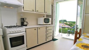 A compact kitchen with a stove, microwave, and cabinets. A balcony with a table and chairs is visible through an open door. - Lovely apartment in Vaux sur Mer (Vaux sur Mer)