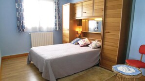 A bedroom with a bed, a wooden wardrobe, a radiator, a lamp, and a small wicker table. - Lovely apartment in Vaux sur Mer (Vaux sur Mer)