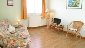 A living room with a floral sofa, a wicker chair, a small table with a lamp, a TV, and a framed picture on the wall. - Lovely apartment in Vaux sur Mer (Vaux sur Mer)