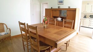 A dining area with a wooden table, six chairs, and a vase with flowers. There is a kitchen in the background with white cabinets and a microwave. - Lovely apartment in Vaux sur Mer (Vaux sur Mer)