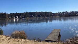 A calm lake with a wooden dock extending into the water, surrounded by houses and trees.