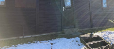 A wooden building with a metal railing on the roof, a door with a number, and a window.