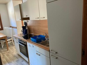 A compact kitchen with a dishwasher, oven, and a coffee maker on the counter. - Fireplace house 30.48 - Waldsee vacation service (Clausthal-Zellerfeld)
