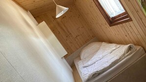 A small, cozy room with a bed, a hanging light fixture, and a window.