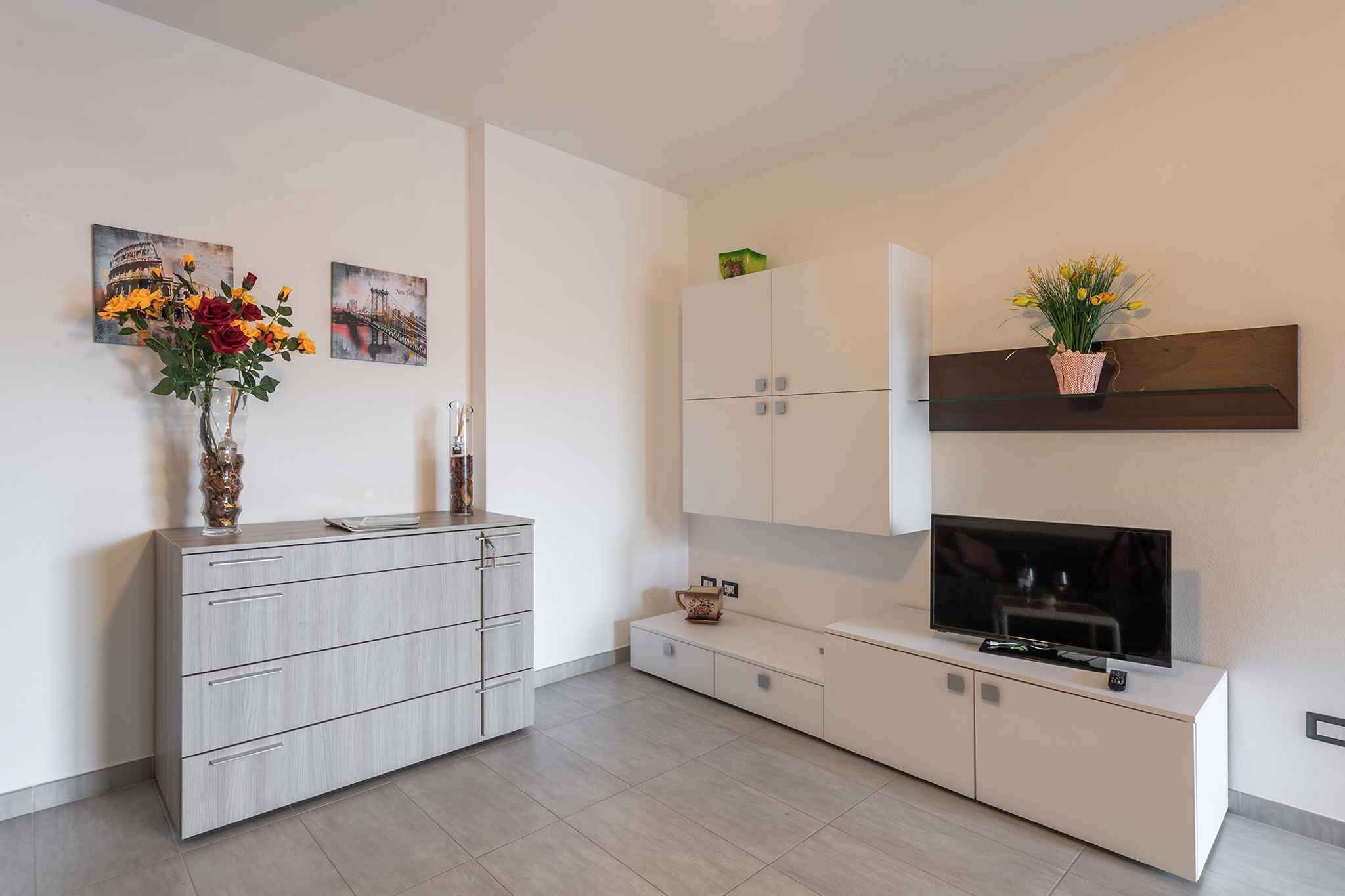 Een moderne woonkamer met een grijze kast, een flatscreen televisie en kunstwerken aan de muur.