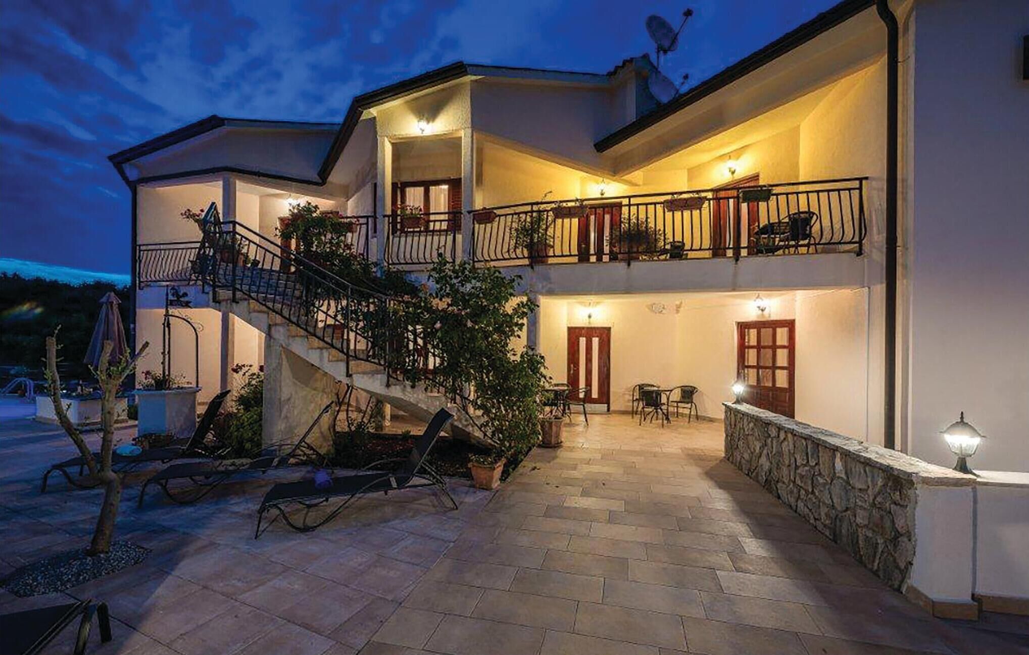 Une maison à deux étages dotée d’un balcon, d’un espace salon extérieur et d’un escalier menant à l’étage supérieur.