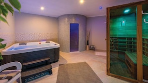 Un cuarto de spa con un jacuzzi, una banca de madera, una camilla de masaje y una puerta de cristal que da a una zona de sauna.
