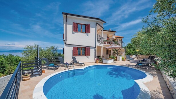 Una casa de dos pisos con piscina, mobiliario exterior y vista al mar.