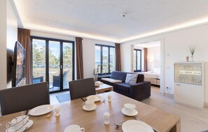 Habitación de hotel moderna con zona de comedor, sofá y vitrina de vidrio con copas.