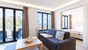 Una sala de estar moderna con un sofá, una mesa de centro y vistas a la playa a través de amplias ventanas.