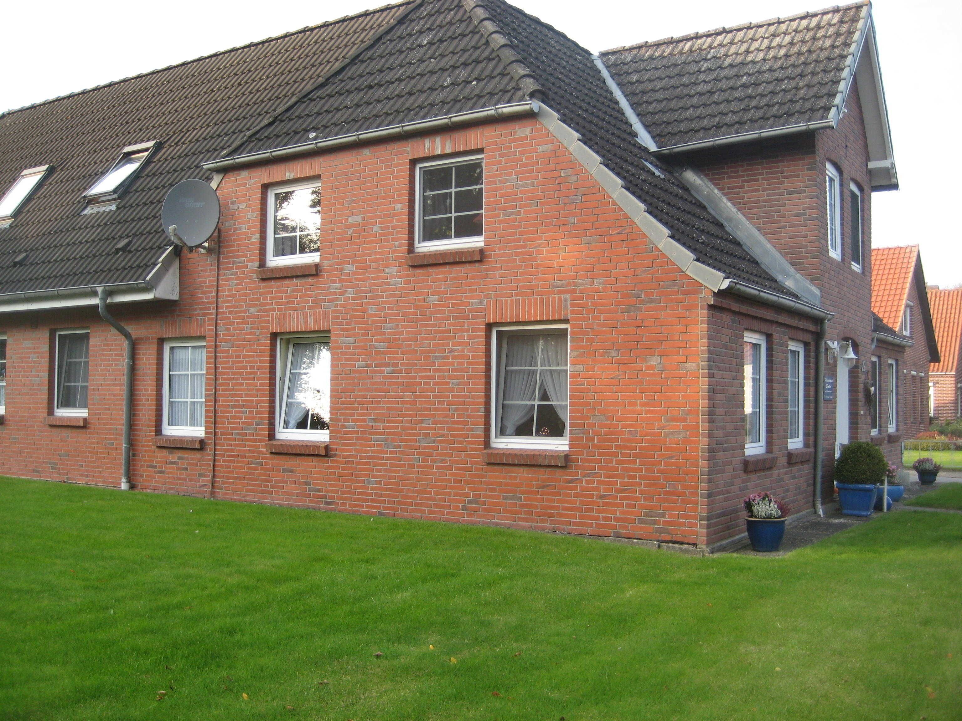Une maison à deux étages, construite en briques, avec un toit en pente, de nombreuses fenêtres et une antenne parabolique.