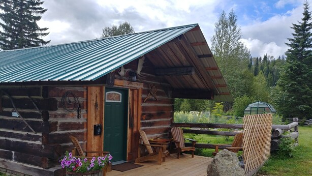 A rustic log cabin with a green door, wooden deck, and outdoor seating area. - Wolfwood Guest Ranch (Clearwater)