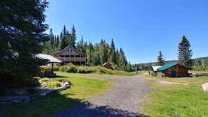 A gravel path leading to a lodge with a porch and a cabin with a green roof. - Wolfwood Guest Ranch (Clearwater)