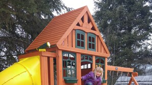 A wooden playhouse with a yellow slide and a window. - Wolfwood Guest Ranch (Clearwater)